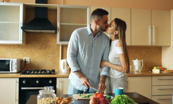 Happy young couple in the kitchen. Handsome man meet and kiss his girlfriend early morning at home