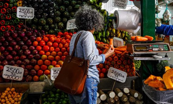 Woman shopping at a vibrant local market stall filled with fresh fruits and vegetables.