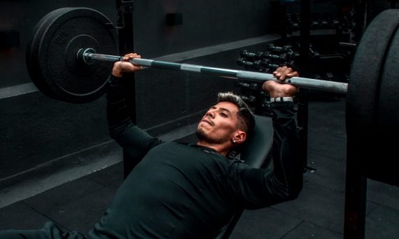 Man performing bench press with heavy barbell in a gym setting, focusing on strength training.